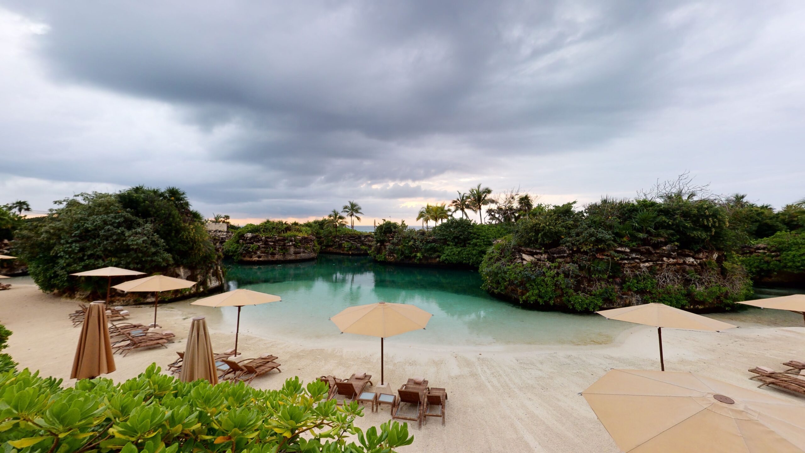 Sandy lagoon beach with umbrellas and loungers ringed by jungle at Hotel Xcaret México