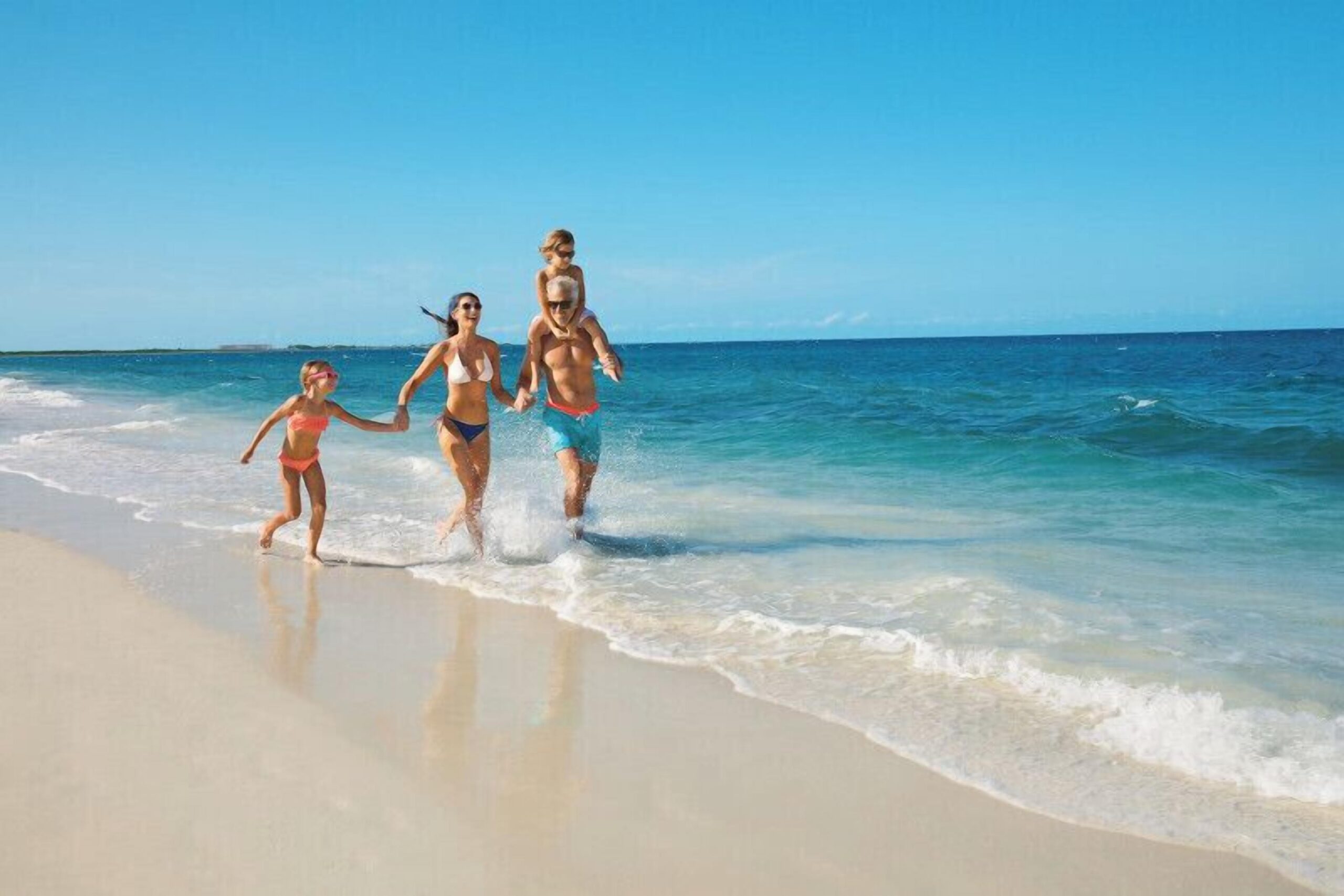 A family walking the soft white-sand beach at the water's edge at Dreams Playa Mujeres