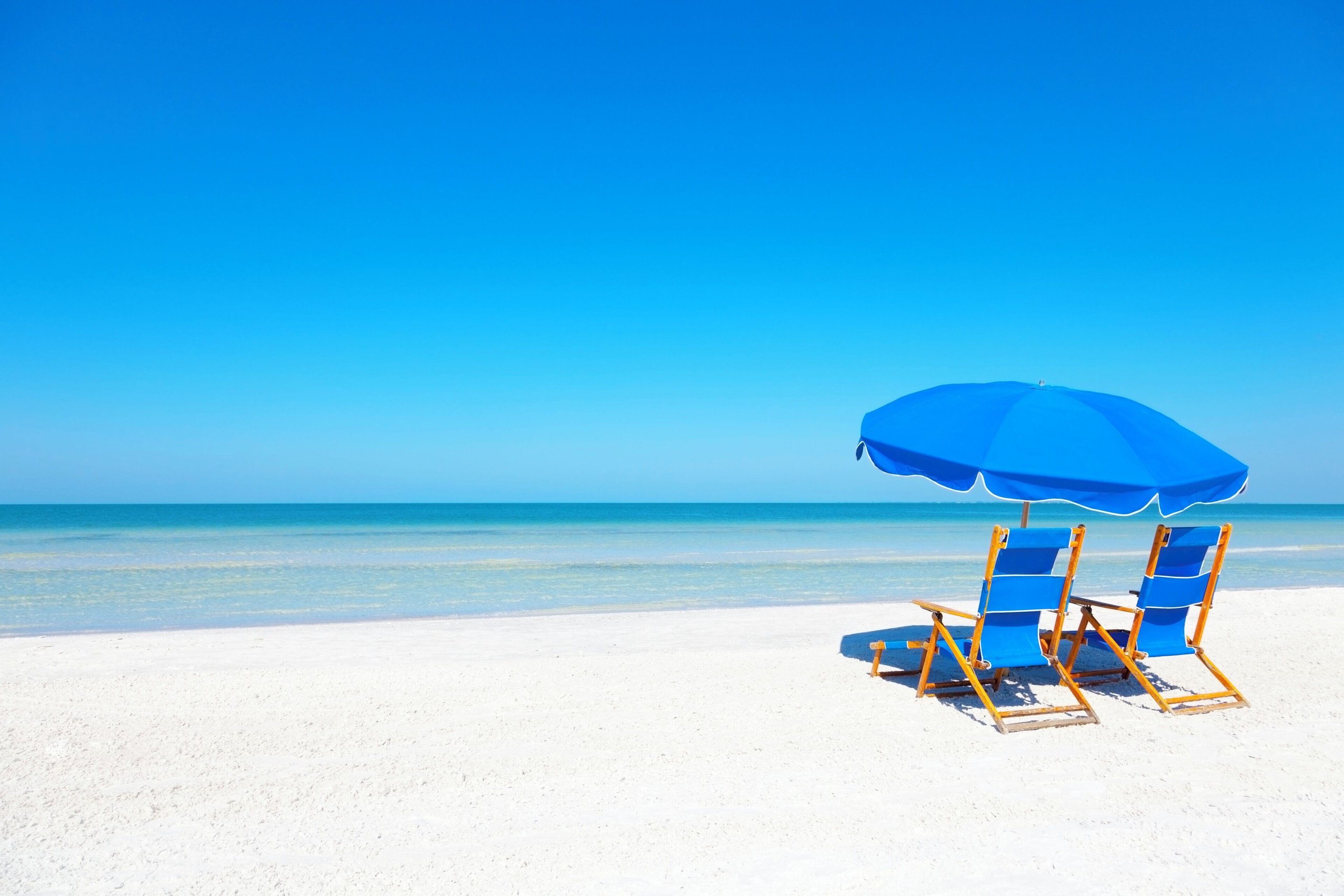 Two blue beach chairs and an umbrella on a white sand Florida ocean beach