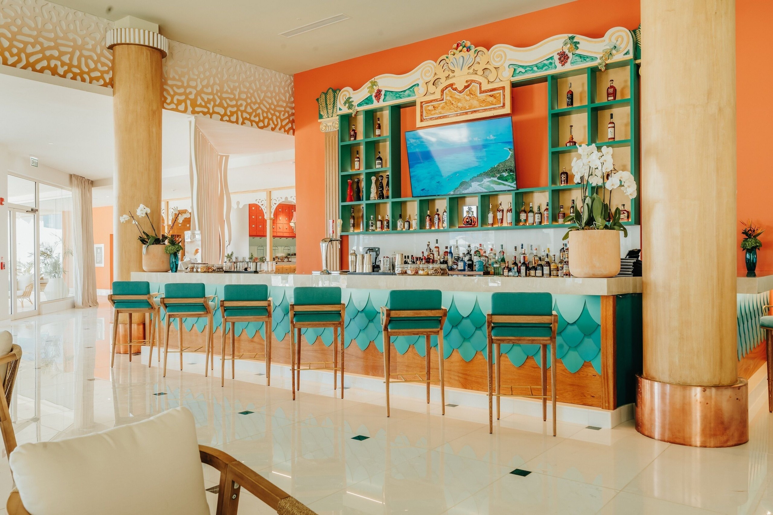 A bar in teal and orange with wooden chairs at JOIA Aruba by Iberostar