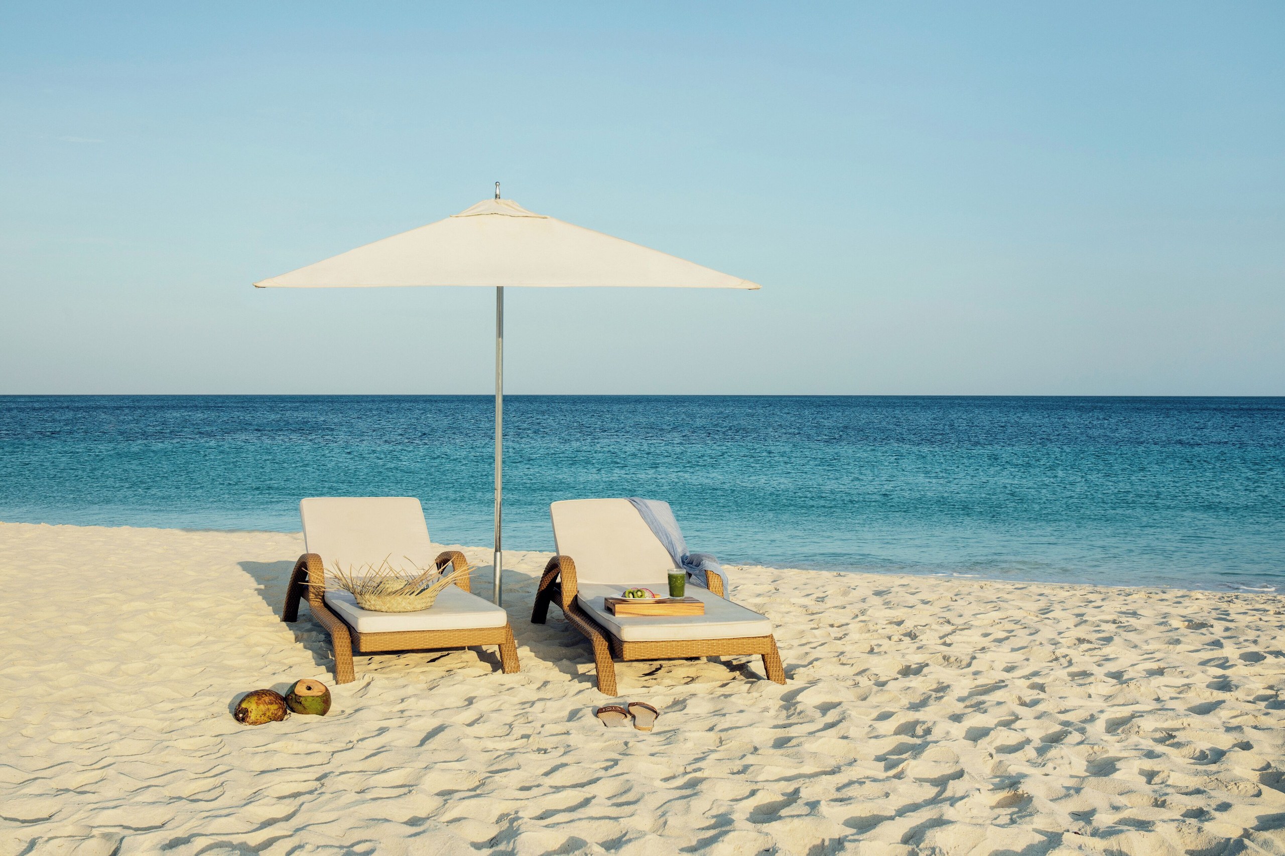 Wicker loungers and a white umbrella on the sand at Eagle Beach, JOIA Aruba by Iberostar
