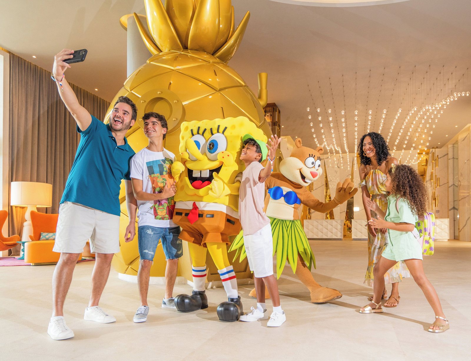 A family taking a selfie with SpongeBob and Sandy Cheeks beside the gold pineapple in the lobby at Nickelodeon Riviera Maya