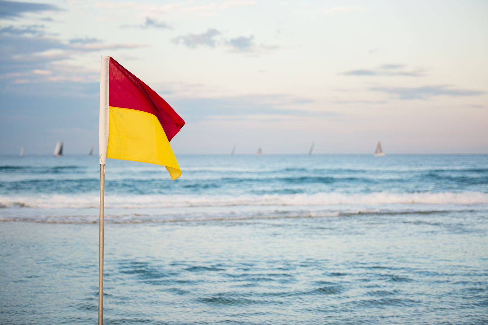 Red and yellow warning flag standing on a beach near the water