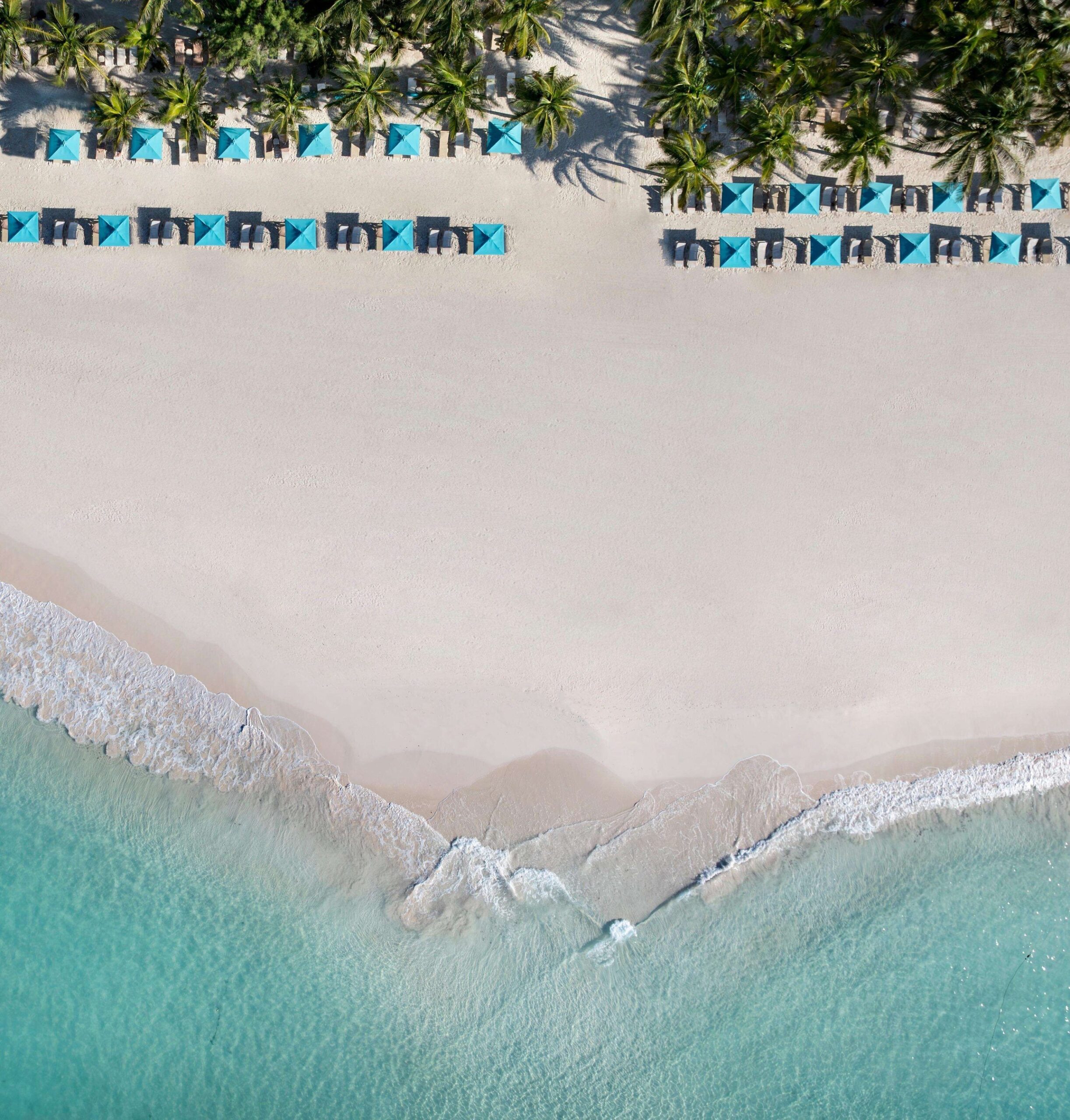 Aerial of Maxwell Beach at Sandals Royal Barbados with white sand, turquoise water, and rows of blue cabanas and loungers