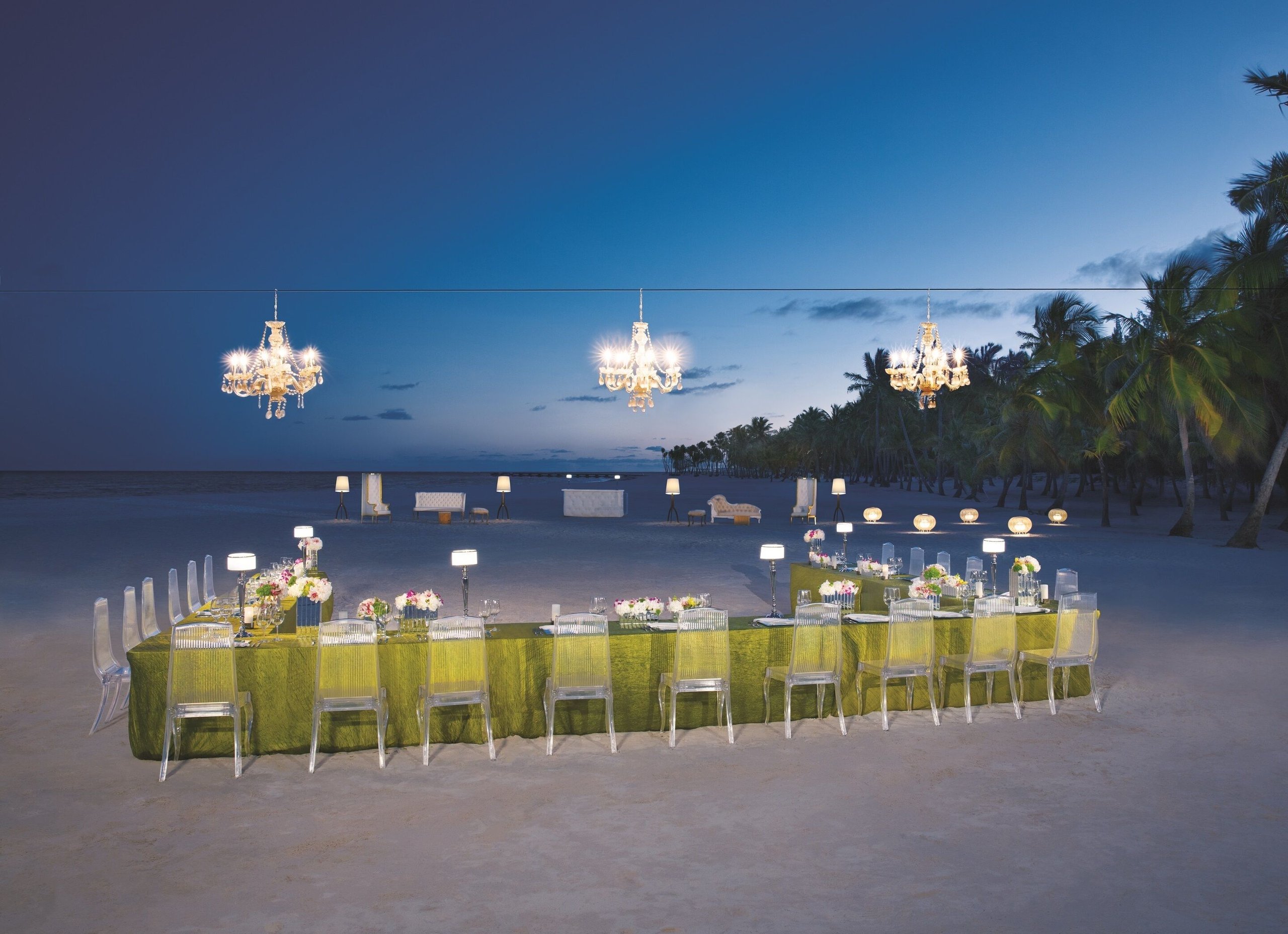 Candlelit dinner table with hanging chandeliers set on the sand at dusk at Secrets Cap Cana