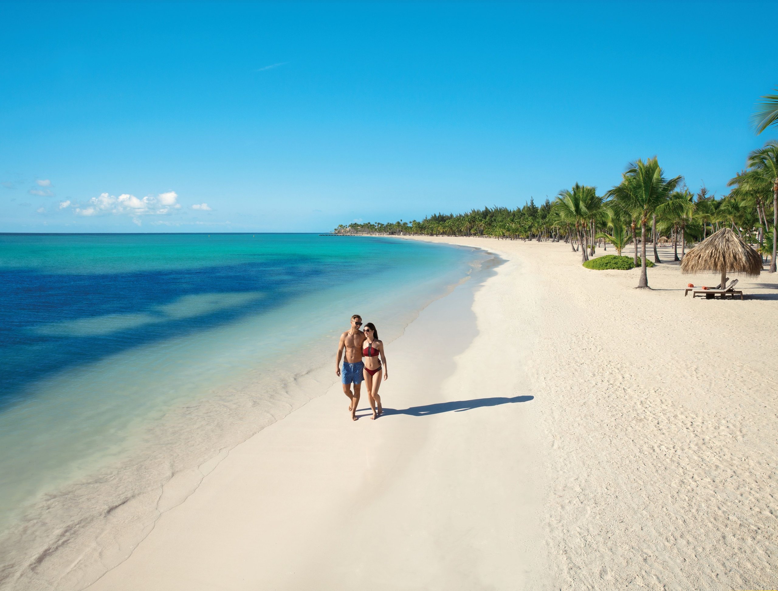 Couple walking the white sand of Juanillo Beach at Secrets Cap Cana with turquoise water and palm trees