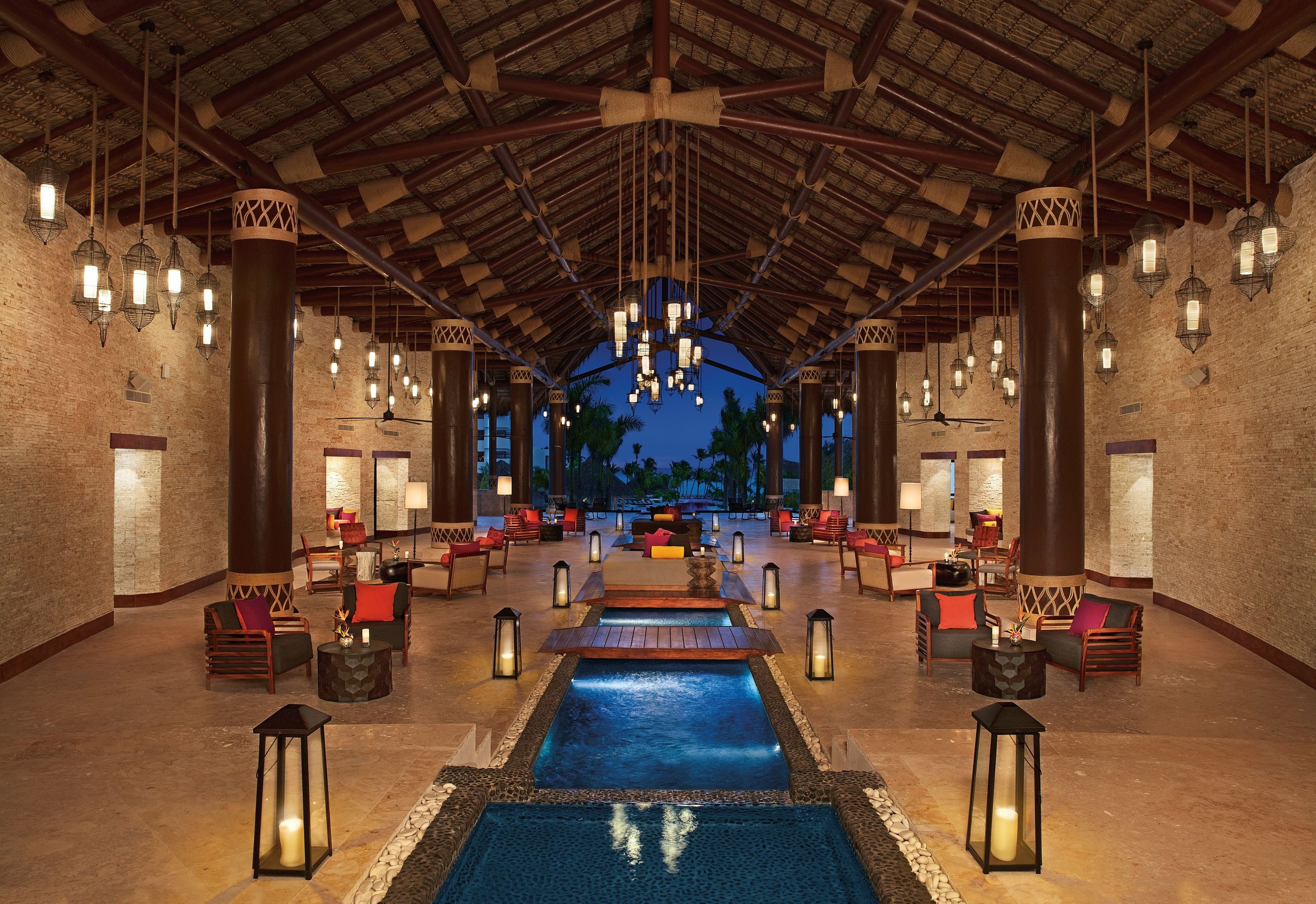 Lantern-lit palapa lobby at Secrets Cap Cana with a central water feature and lounge seating at dusk
