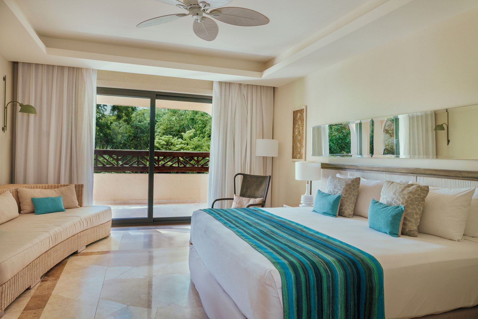 A guest room at Catalonia Royal Tulum with a bed, a sofa and a balcony onto the garden