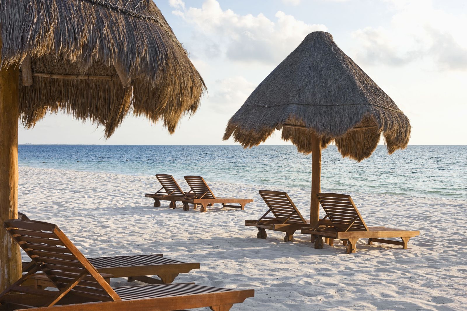 Wooden loungers under palapa umbrellas on the calm beach at Excellence Playa Mujeres