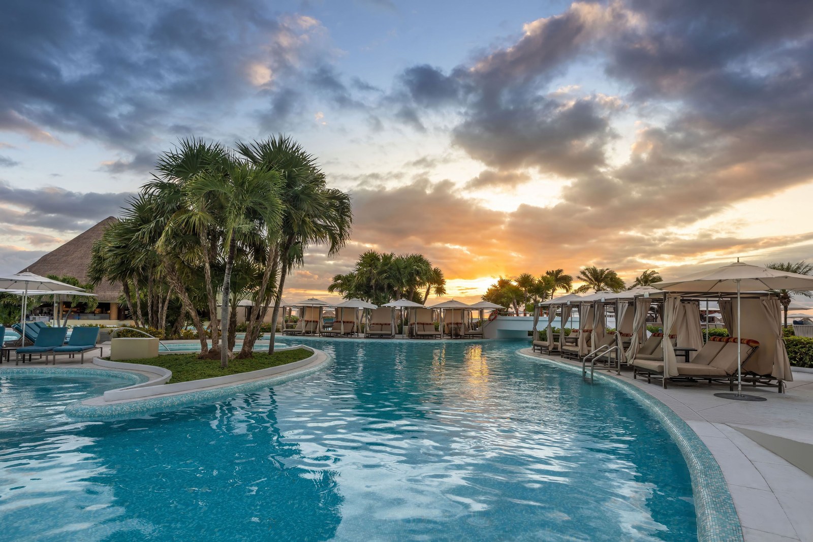Pool at Moon Palace Cancún at sunset with palm trees and cabanas