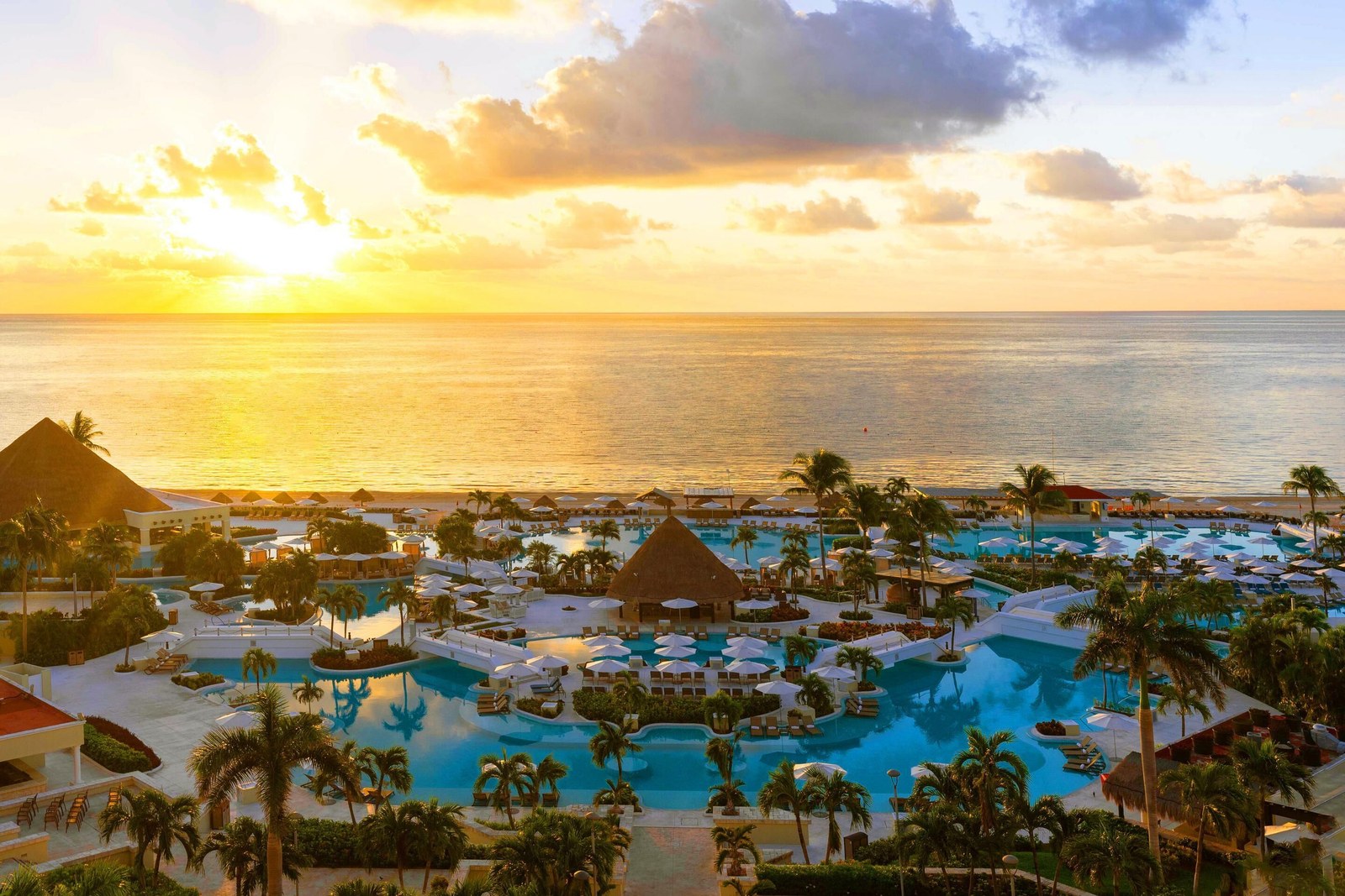 Aerial view of Moon Palace Cancún at sunset with the pools lit and the sea behind