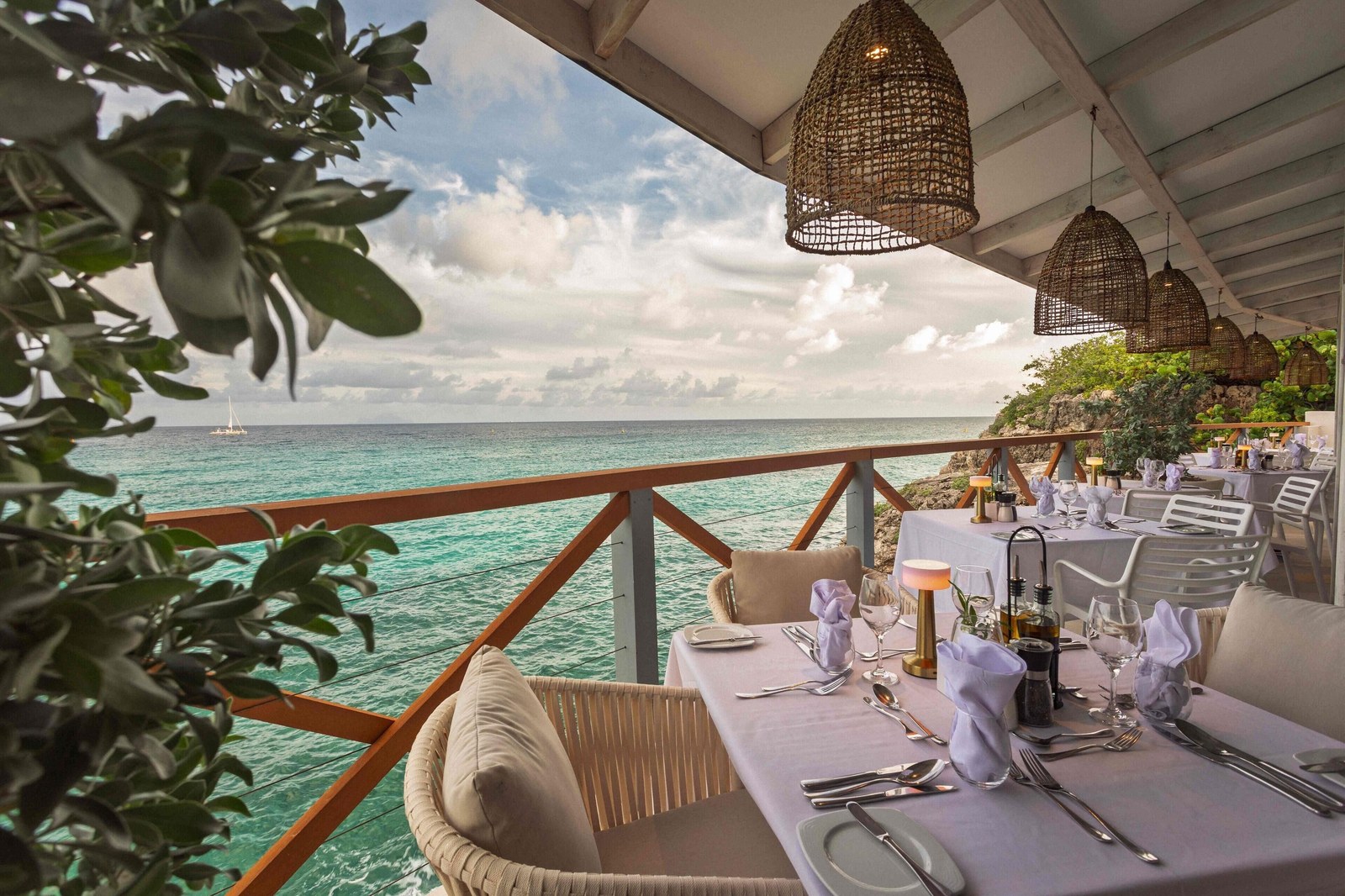 A set dinner table on the Azul restaurant terrace at Sonesta Ocean Point, with the sea below and rattan lamps above