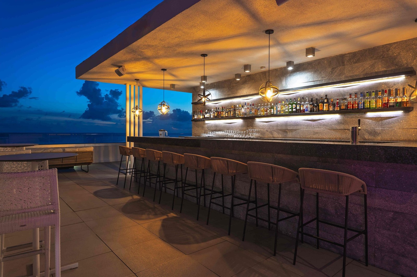 The Sunset Lounge rooftop bar at Sonesta Ocean Point at dusk, with bar stools along the counter and the sky behind