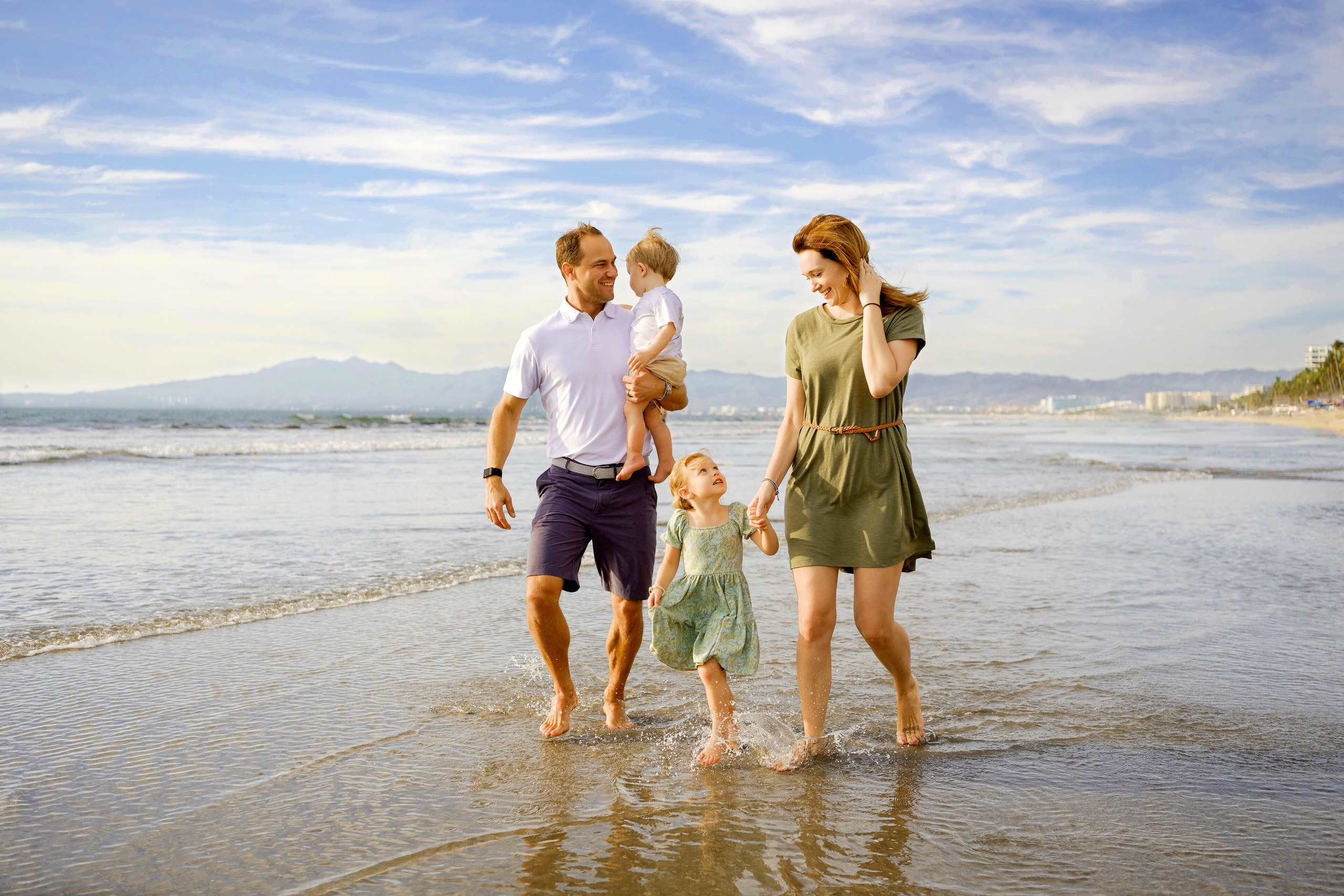 A family walking along the wide sandy beach in front of Grand Velas Riviera Nayarit