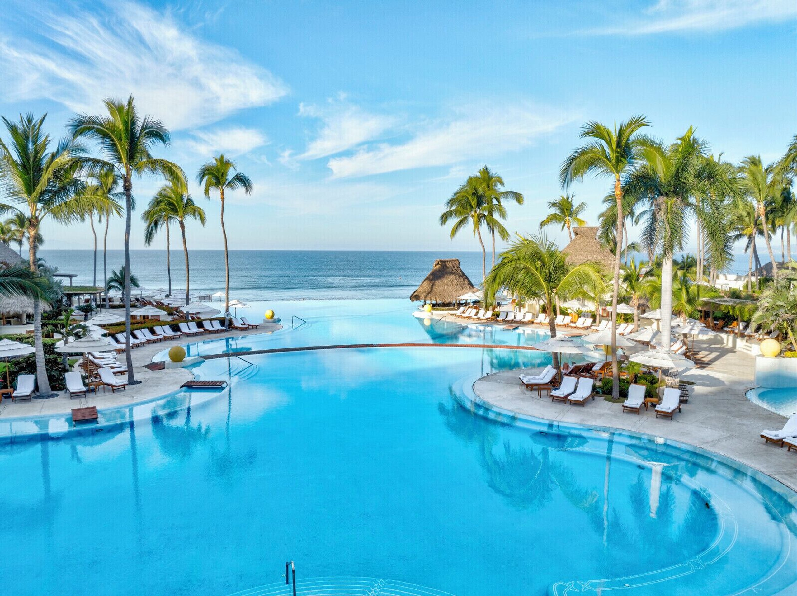 The infinity pool at Grand Velas Riviera Nayarit with lounge chairs, palm trees and the ocean behind it